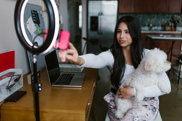 A woman vlogging at home using a smartphone and ring light, holding her pet dog.