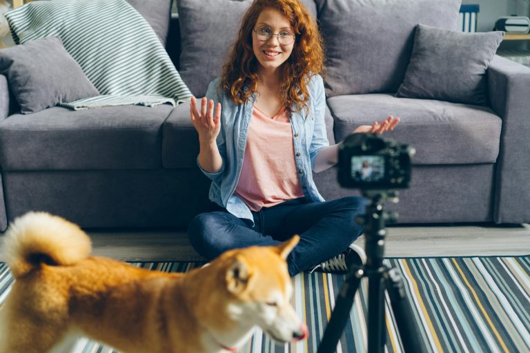 Redheaded woman filming a video at home with her dog. Cozy living room setting.